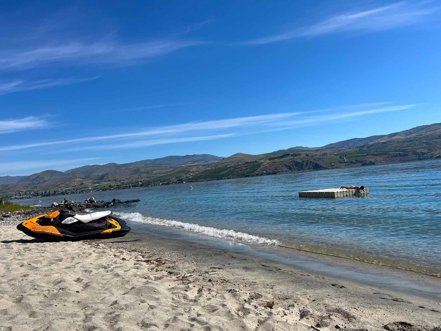 Sandy-Waterfront-beach-on-Lake-Chelan-wa-with-floating-dock-and-orange-and-white-jetski